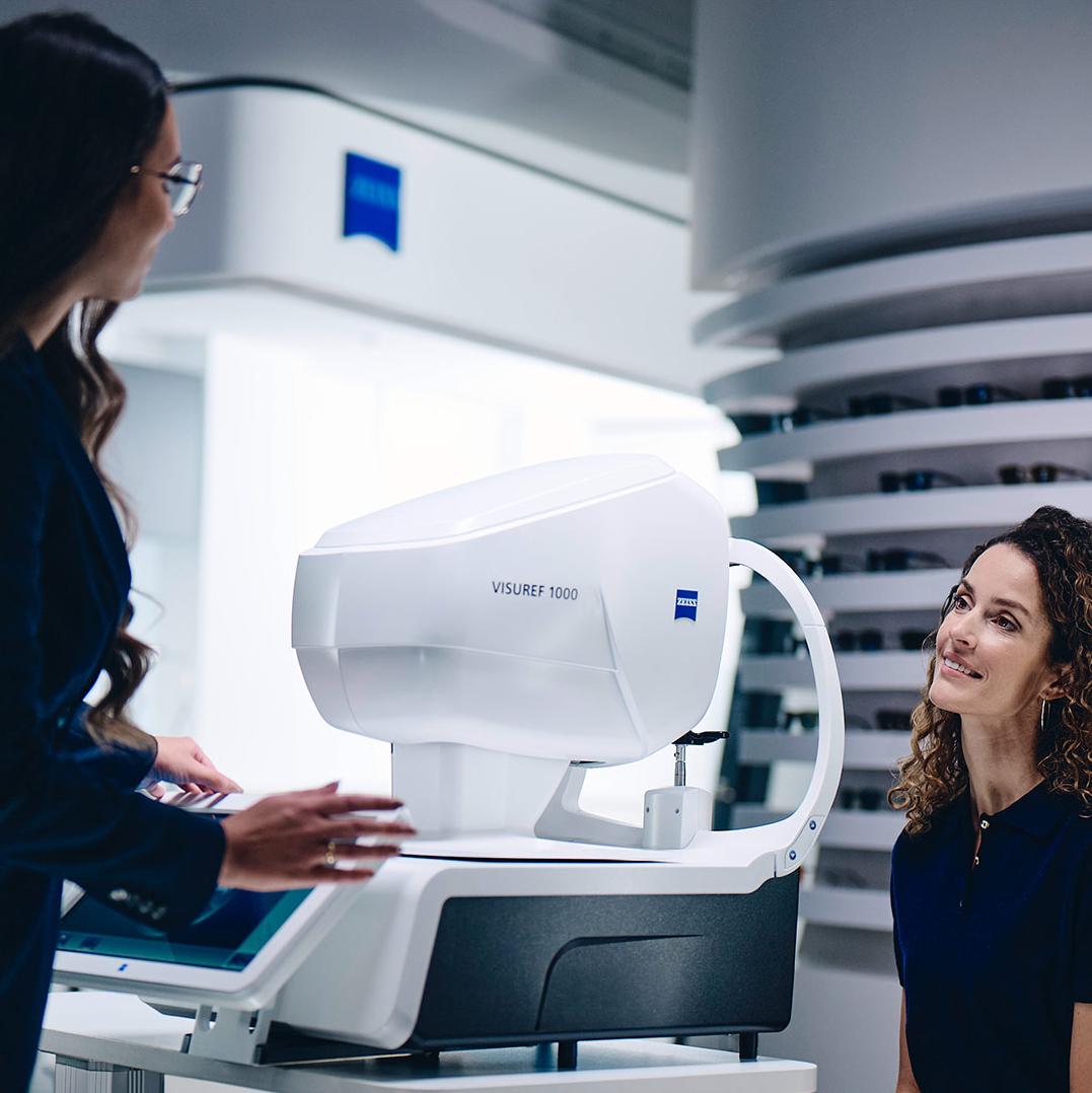 A woman sitting in front of the ZEISS VISUREF 1000 looking at a female optician.